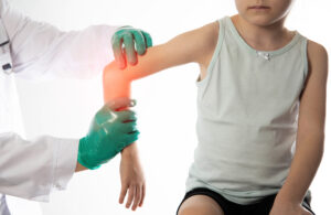 The hands of a traumatologist doctor in green medical gloves examine the girl s damaged elbow joint. Injury and dislocation of the elbow joint, bruise and fracture. Growing pains